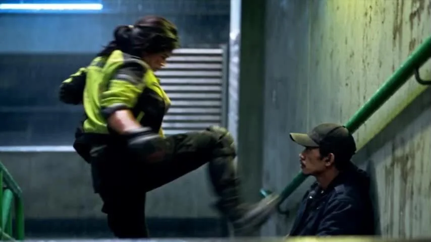 Lia kicks the Driver on the stairwell landing beside a green railing