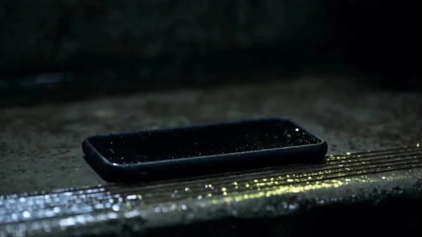 A smartphone lies on a wet concrete step, screen dark