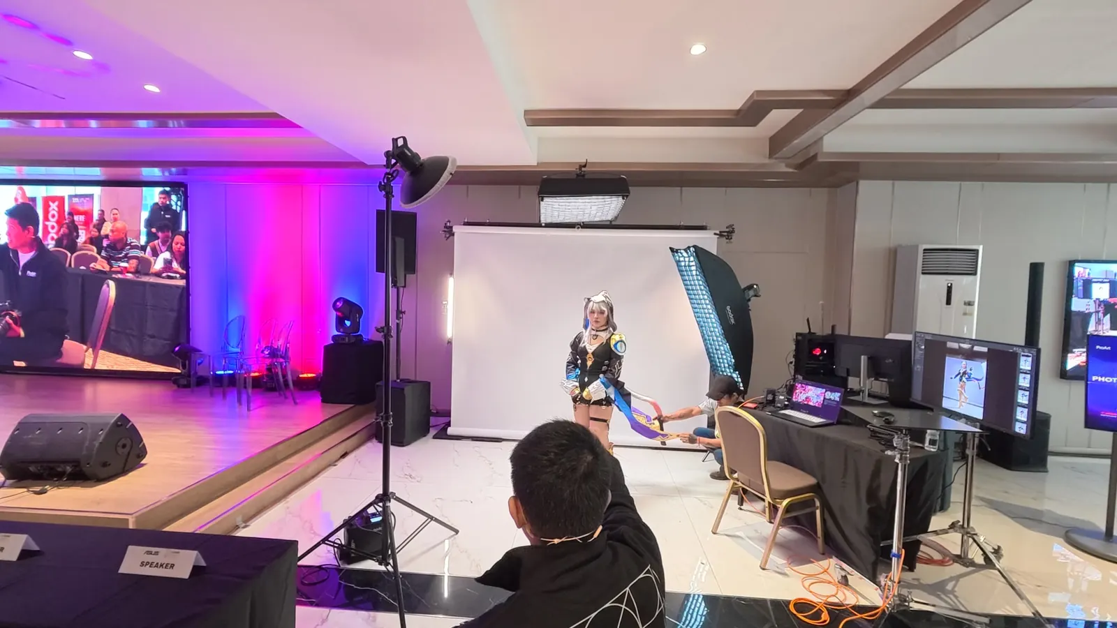 Live cosplay photo shoot on a white backdrop with lighting and monitors