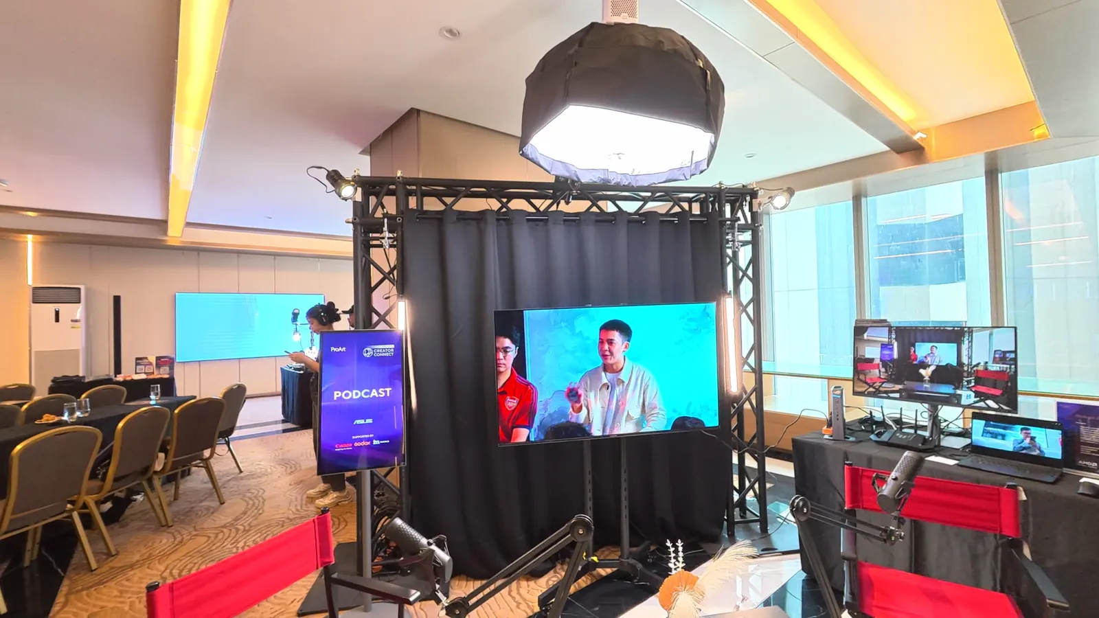 Podcast zone with red director chairs, microphones and a live multicam feed on a large screen